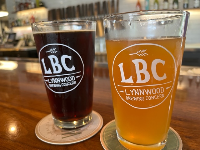 two pint glasses of beer on a bar; taps in the background