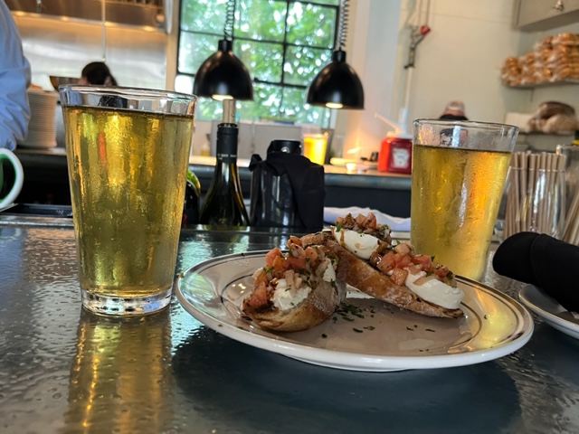 two pint glasses of beer, with crostini appetizers on a plate in between