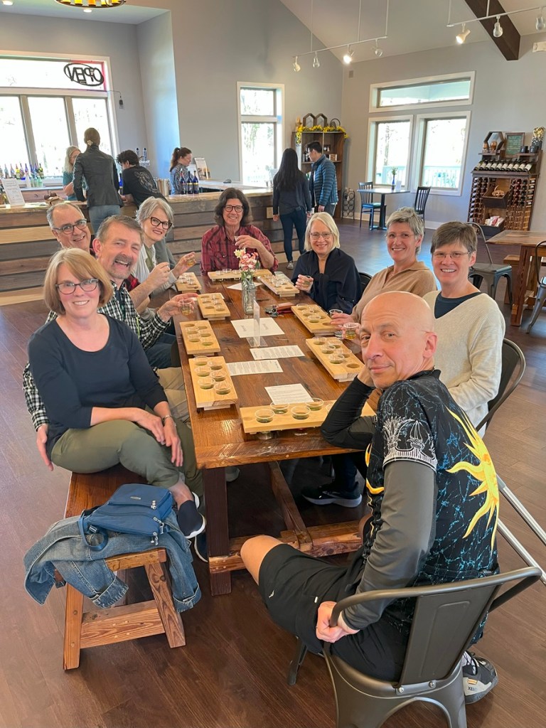 Group of nine people sitting around a wooden table with wine flights in front of them