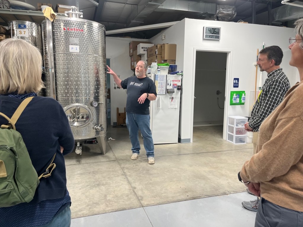 Mead maker stands beside large, stainless tank for fermenting mead