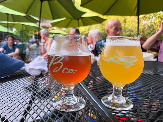 two glasses of beer sitting on an outdoor table, with blurred background