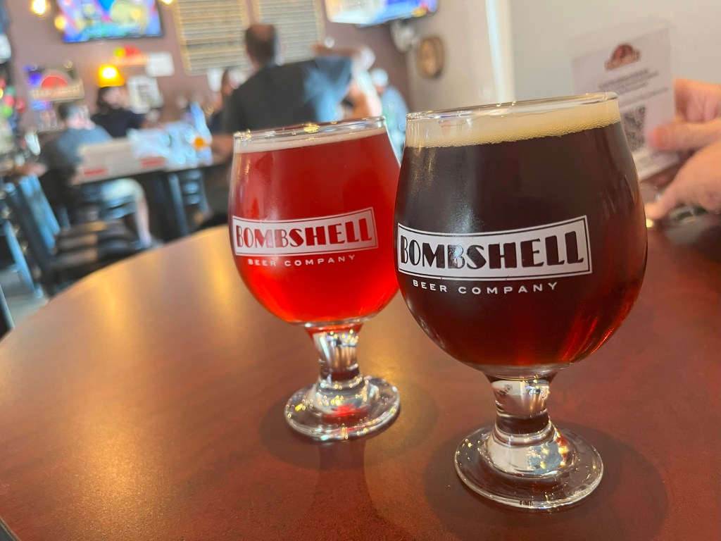 Two Bombshell Beer glasses with beer, on table, with taproom in background