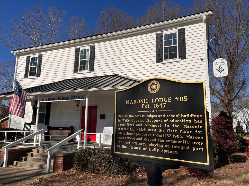 front view of lodge, white wood building, black shutters, historic sign in foreground